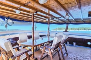 Überdachtes Deck des Schiffes San Snova mit Holztisch, Stühlen mit Kissen und Panoramablick auf kroatische Küste und blaues Meer.