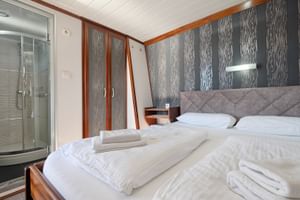 Doppelkabine auf MY Magellan mit grau gepolstertem Bett, weißer Bettwäsche, gefalteten Handtüchern, gemusterten Wandpaneelen und Glasduschkabine.