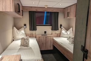 Zweibettkabine auf dem Hauptdeck der MS Princess mit zwei Einzelbetten, weißer Bettwäsche, Holzverkleidung, Staufächern, Fenster mit Vorhängen und Leselampen.