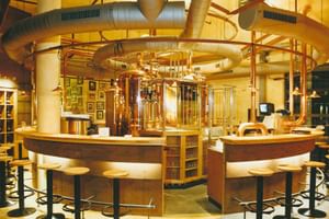 Runde Bar mit kupfernen Braukesseln im Hammerbräu. Barhocker umgeben die Theke mit sichtbarer Brauanlage und Kupferrohren darüber.