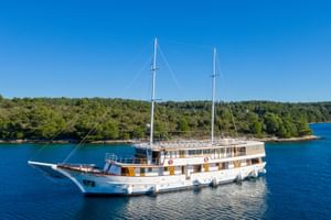 Weiße Motoryacht MY Magellan mit zwei Masten vor bewaldeter kroatischer Küste im ruhigen blauen Wasser unter klarem Himmel.