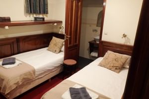 Kompakte Zweibettkabine mit zwei Einzelbetten, Holzmöbeln und sichtbarem Bad durch offene Tür auf SIMMER FAN FRYSLÂN.