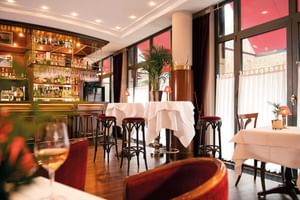 Innenraum der CHEZ VICTOR'S Bar mit Holztheke voller Flaschen, weiß gedeckten Tischen, dunklen Holzstühlen und großen Fenstern.