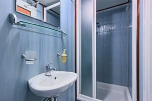 Kompaktes San Snova Schiffsbadezimmer mit weißem Waschbecken, Glasduschkabine mit blauen Fliesenwänden, Spiegel und Handtuchhalter.