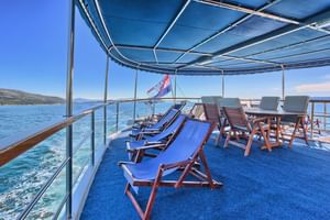 Oberdeck der San Snova mit blauen Liegestühlen und Esstisch unter Sonnendach, mit Blick auf türkises Meer und kroatische Küste.