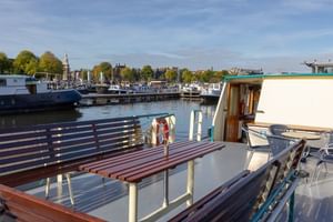 Sun deck of MS Flora with wooden benches and white railings overlooking a marina with boats and historic buildings under blue sky.
