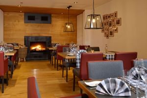 Gemütliches Restaurant mit gedeckten Tischen, rot-grauen Polsterstühlen, Holzboden, brennendem Kamin und Pendelleuchten im Landhotel Schnuck.