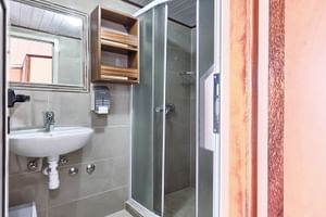Compact bathroom on MY Andela Lora with white sink, mirror, wall cabinet, and glass shower enclosure with gray tiles.