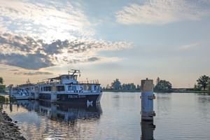 Weißes Flusskreuzfahrtschiff MS Princess im Hafen Schwedt bei Morgendämmerung. Ruhiges Wasser spiegelt das Schiff und den Himmel mit vereinzelten Wolken.