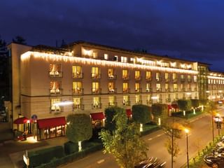 Außenansicht des Victors Residenz Hotels bei Nacht mit warmer Beleuchtung, mehreren Stockwerken mit beleuchteten Fenstern, roten Markisen.