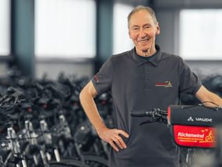 Thomas Brandhorst in dark polo shirt standing with a Vaude bicycle with red Rückenwind bag in a bike storage facility.