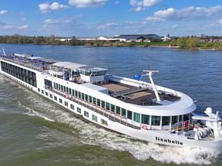 Weißes Flusskreuzfahrtschiff MS Lisabelle fährt auf blauem Wasser mit Kielwasser dahinter. Das Schiff hat mehrere Decks und grün getönte Fenster.