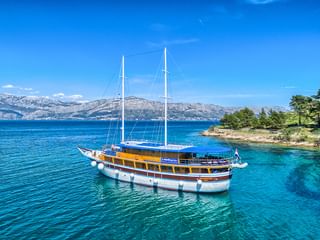 San Snova, ein zweimastige Segelschiff mit weißem Rumpf und Holzdeck, vor Anker im türkisfarbenen Adriatischen Meer vor Kroatien.