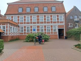 Frau namens Olga mit Fahrrad vor historischem rotem Backsteinrathaus in Bad Bederkesa mit weißen Fenstern und Ziegeldach.