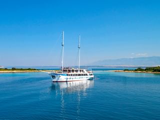 Weiße Motoryacht MS Aria mit zwei Masten vor Anker in ruhigen blauen Gewässern vor der kroatischen Küste mit grünen Inseln und Bergen.