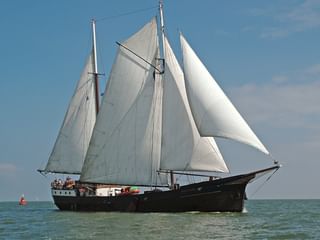 Traditionelles zweimastiges Segelschiff Wapen fan Fryslan mit weißen Segeln auf ruhigem blauen Wasser unter teilweise bewölktem Himmel.