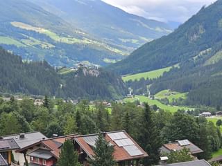 Panoramic view of the Tauern valley showing traditional Alpine houses with red tile roofs in foreground, green meadows and forested mountains.