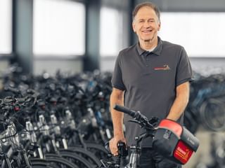 Achim Wendland im grauen Poloshirt steht mit Fahrrad in großer Lagerhalle mit Fahrradreihen im Hintergrund.
