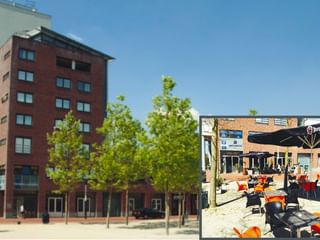 Rotes Backsteingebäude des Fehn City Hotels in Stadskanaal mit Außenterrasse. Modernes mehrstöckiges Hotel mit jungen Bäumen.