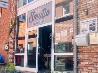 Backsteingebäude mit Eingang zum Hotel Smutje. Weißes Schild zeigt 'Stadthotel-GmbH'. Zwei Personen sitzen auf einer Bank vor dem Eingang.