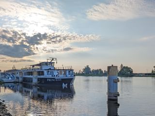 Weißes Flusskreuzfahrtschiff MS Princess im Hafen Schwedt bei Morgendämmerung. Ruhiges Wasser spiegelt das Schiff und den Himmel mit vereinzelten Wolken.