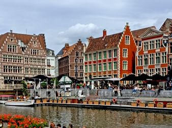 Reihe bunter mittelalterlicher Gildenhäuser mit Treppengiebeln entlang eines Kanals in Brügge, Belgien. Touristen versammeln sich auf Uferterrasse.