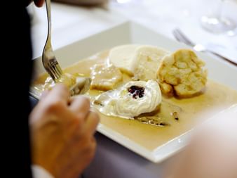 Person schneidet in einen Dessertteller mit Vanillesauce, Eis mit Beerentopping und Gebäck im Hotel Ludmila in Mělník.