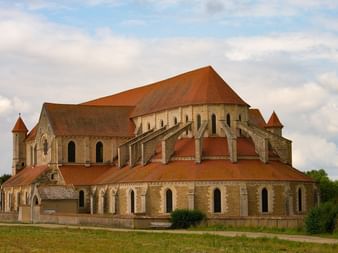 Abtei Pontigny mit romanischer Architektur, großer Apsis mit Terrakottadach und Strebepfeilern, inmitten einer grünen Wiese im Burgund.