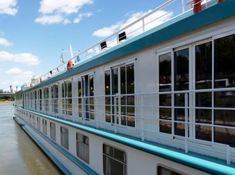 Weißes Flusskreuzfahrtschiff MS Switzerland mit türkisfarbenen Akzenten und großen Fenstern am ruhigen Fluss unter blauem Himmel.