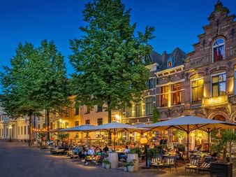Historische niederländische Gebäude mit Treppengiebeln an einem Platz in Deventer in der Dämmerung. Außenterrasse mit Gästen unter Schirmen.