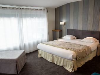 Modernes Hotelzimmer im Grand Hotel Toulouse mit Doppelbett, grauem Kopfteil, gestreifter Tapete, Nachttischlampen und Einzelbett am Fenster.