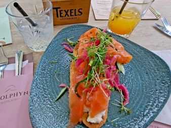 Geräucherter Lachs auf Fladenbrot mit Frischkäse, Sprossen und eingelegtem Gemüse auf blauem Teller im Bistro Dolphyn in Middelburg.