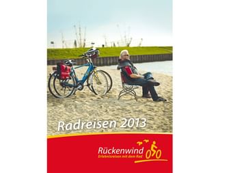 Cover des Rückenwind Radreisen Katalogs 2013 zeigt Person auf Strandstuhl neben Tourenrad mit roten Taschen am Sandstrand.
