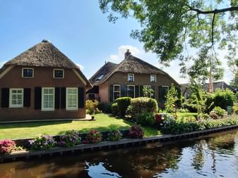 Traditionelle niederländische Reetdachhäuser mit grünen Rasenflächen und Blumengärten entlang eines Kanals in Giethoorn.