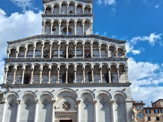 Weiße Marmorkirche mit mehreren Ebenen von Bogengalerien und Säulen vor blauem Himmel mit weißen Wolken in der Toskana, Italien.
