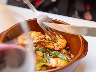 Terrakotta-Schale mit gegrillten Garnelen und Gemüse, serviert mit Gabel und Messer im Restaurant des Grand Hotel Toulouse.