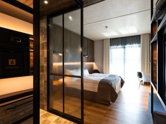 Modernes Hotelzimmer im Hotel Zollhaus Rastede mit Glastrennwand, Holzboden, weißem Bett und stimmungsvoller Beleuchtung.