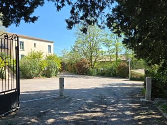 Open entrance gate with decorative ironwork leading to Ceres Boutique Hotel and Spa in Provence, showing a gravel driveway, trees, and a beige building.