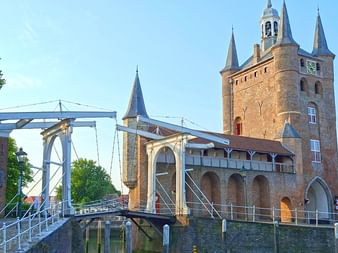 Mittelalterliches Backsteintor mit mehreren Türmen und Glockenturm in Zierikzee, verbunden mit einer weißen Zugbrücke über einem Kanal.