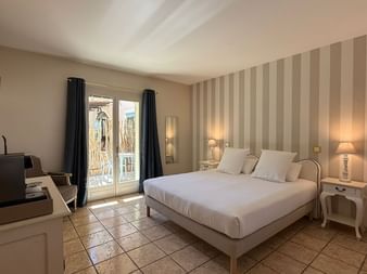 Helles Hotelzimmer mit Doppelbett, gestreifter Akzentwand, Terrakottafliesenboden, Balkontür, Nachttischlampen und Kaffeemaschine im Ceres Boutique Hotel.