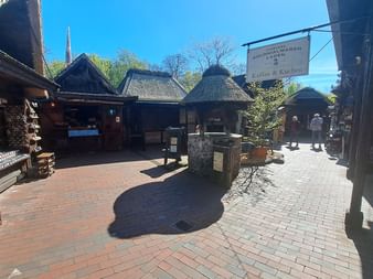 Innenhof mit traditionellen reetgedeckten Räucherhäusern in Bad Bederkesa. Ziegelpflaster, Holzgebäude und Besucher unter blauem Himmel.