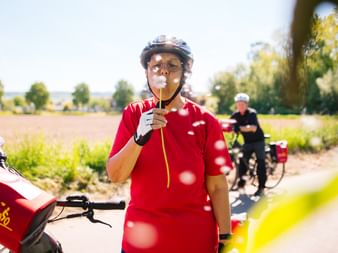 Radfahrer in rotem Shirt und Helm genießt Eis auf ländlichem Weg bei Höxter, mit anderem Radfahrer im Hintergrund und grünen Feldern.