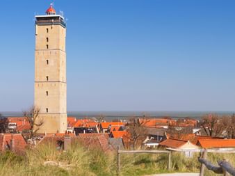 Hoher beiger Leuchtturm mit rotem Dach überragt das Dorf Terschelling mit traditionellen holländischen Häusern mit orangeroten Ziegeldächern.