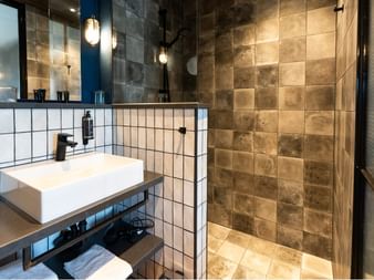 Zeitgenössisches Badezimmer mit weißem rechteckigem Waschbecken, großem Spiegel, begehbarer Dusche mit braunen Fliesen im Hotel Zollhaus Rastede.