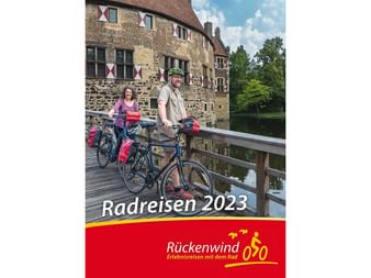 Zwei Radfahrer mit Tourenrädern auf einer Holzbrücke vor einer historischen Steinburg mit Wassergraben. Cover des Rückenwind Radreisen-Katalogs 2023.