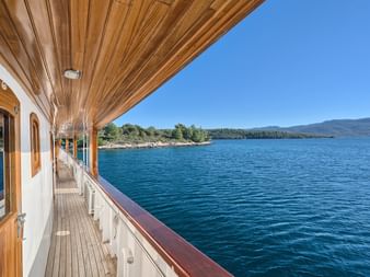 Blick vom Holzdeck der MY Magellan mit weißer Reling auf das blaue Adriatische Meer, grüne Küste und Berge unter klarem Himmel in Kroatien.