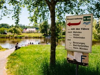 Weserradweg R99 Schild am Weserufer bei Wehrden mit Richtungsangaben zu verschiedenen Orten und Fährverbindungen.