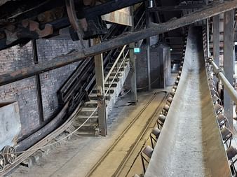 Industrielles Förderbandsystem auf Zeche Zollverein mit Backsteinmauern, Metallkonstruktionen und Treppen in historischer Bergbauanlage.