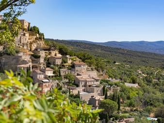 Stone village of Gordes built on a hillside in Provence, with traditional houses cascading down the slope surrounded by green vegetation.