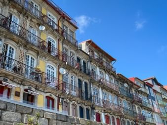 Reihe bunter historischer Gebäude mit verzierten Eisenbalkonen am Cais da Estiva im Douro-Tal von Porto vor strahlend blauem Himmel.